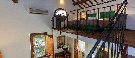 Une pièce à plusieurs niveaux avec un escalier en bois, un coin repas comprenant une table et des chaises, et un lit avec une literie verte.