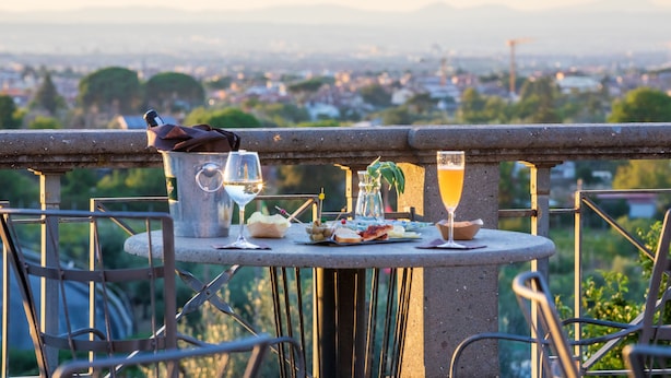 A table with a bottle, glasses, and food, overlooking a cityscape.