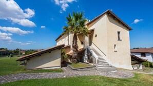 A two-story building with a stone staircase leading to the entrance, surrounded by a well-maintained lawn and a palm tree.