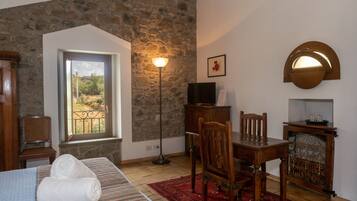 Une pièce avec un mur en pierre, une table à manger en bois, un téléviseur posé sur un meuble en bois, un tapis rouge et une fenêtre donnant sur un paysage verdoyant.
