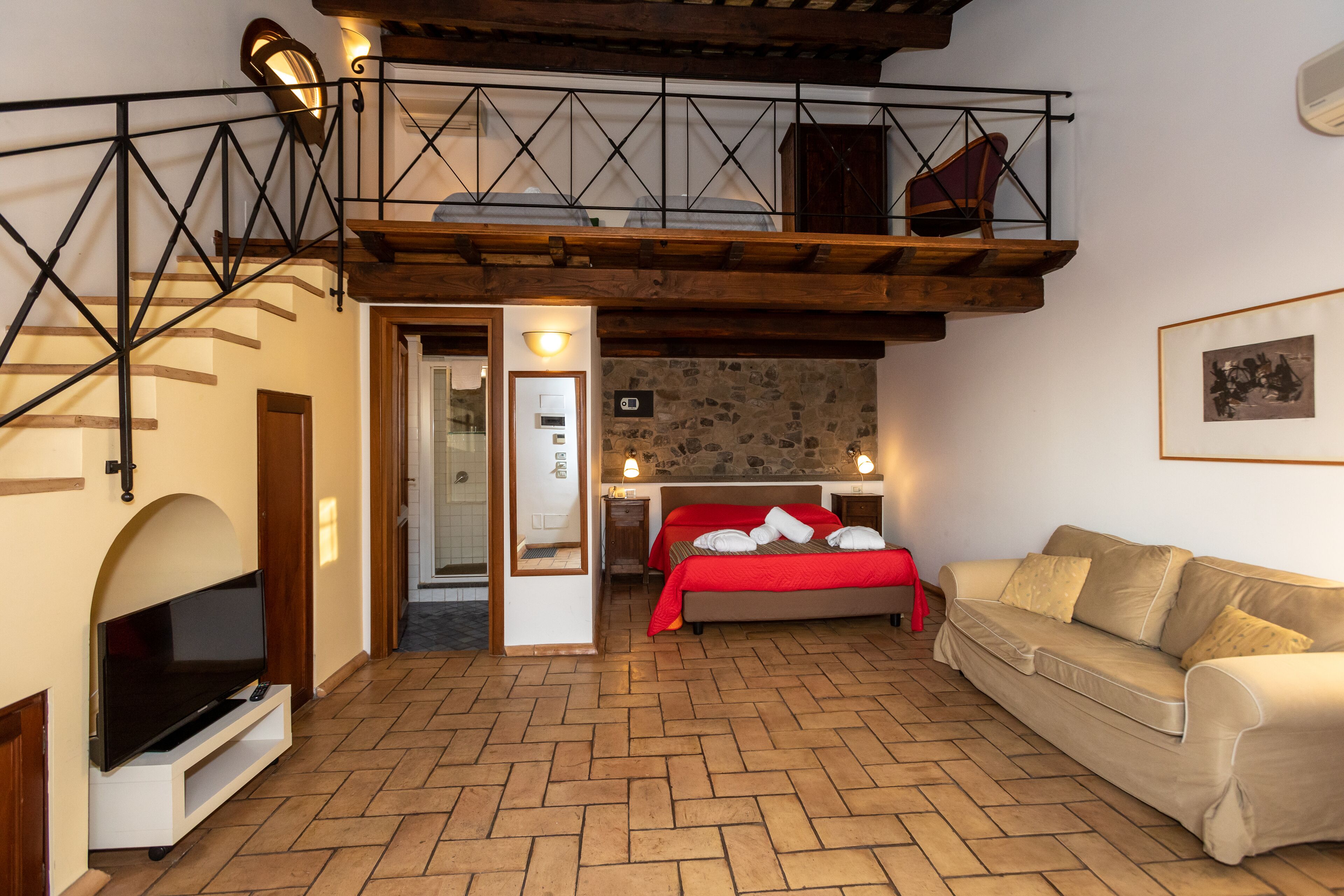 A hotel room with a loft bed, a sofa, a TV, and a stone wall.