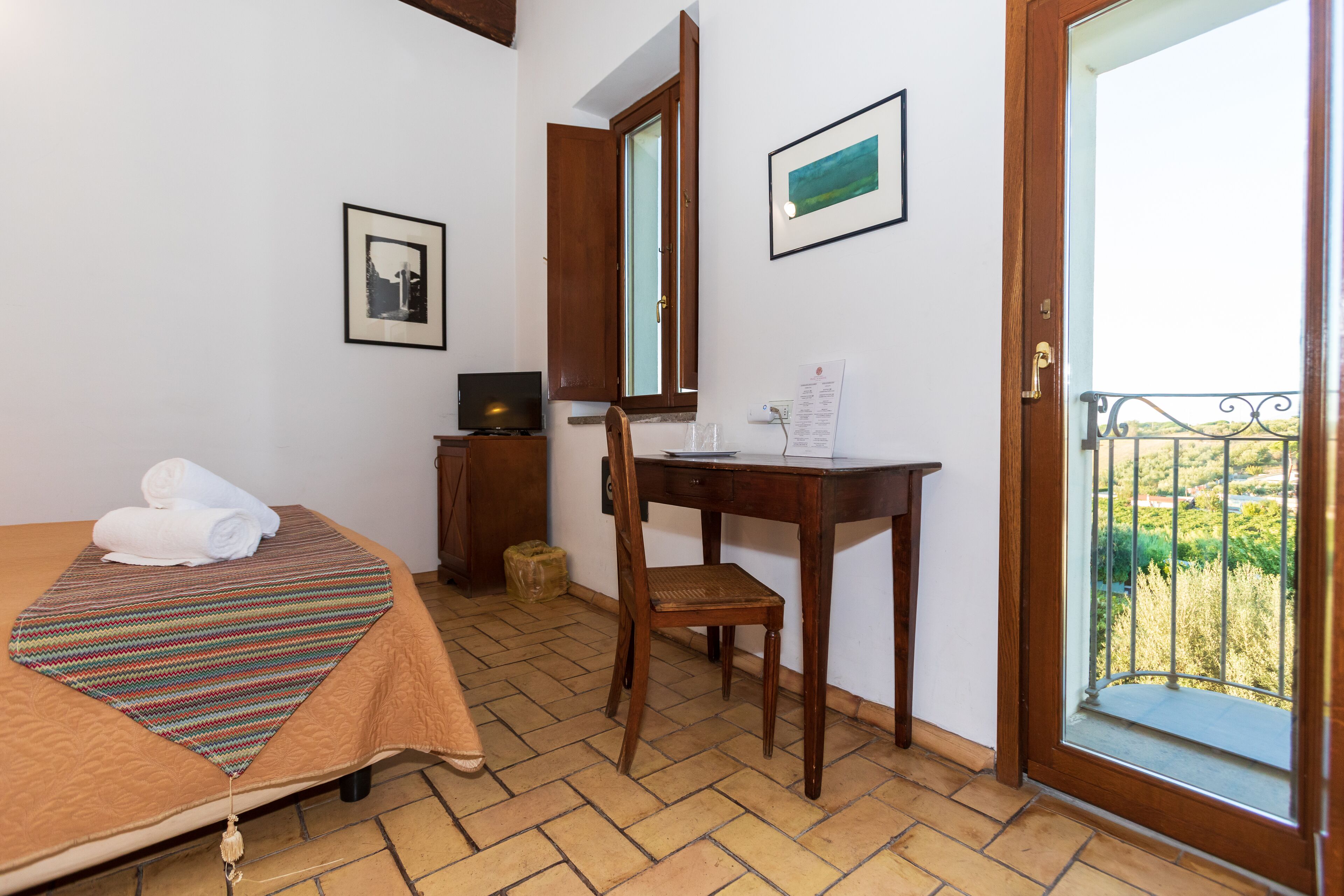 A bedroom with a bed, a desk, a chair, a television, and a balcony with a view.