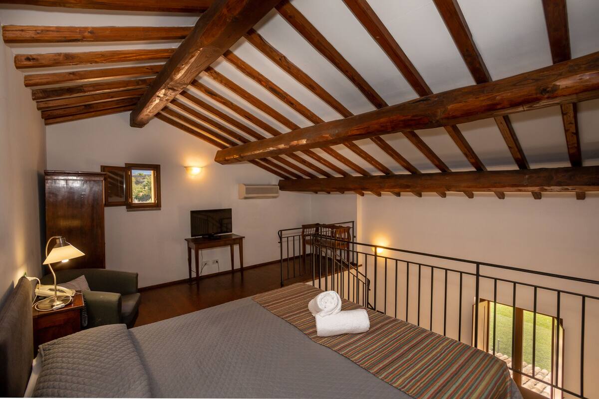 Ein Schlafzimmer mit Bett, Schreibtisch, Stuhl, Lampe und einem Balkon mit Geländer.