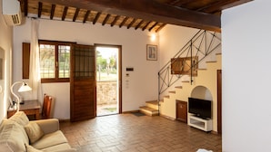 A spacious room with a wooden ceiling, a sofa, a bed with a red blanket, a television, and a staircase leading to an outdoor area.