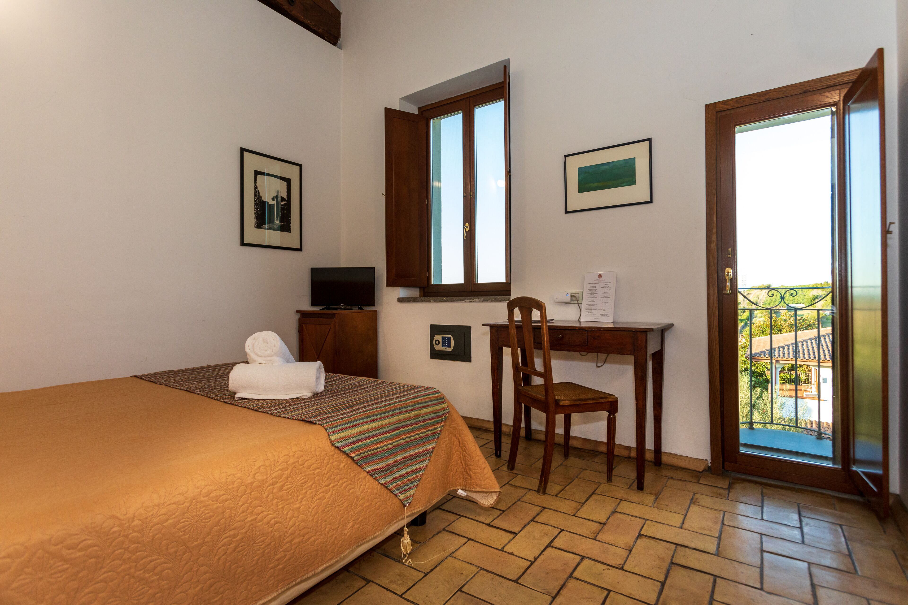 A hotel room with a bed, a desk, a chair, a television, and a balcony with a view.