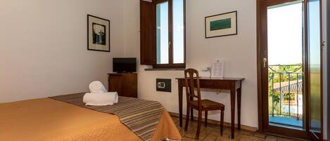 A hotel room with a bed, a desk, a chair, a television, and a balcony with a view.