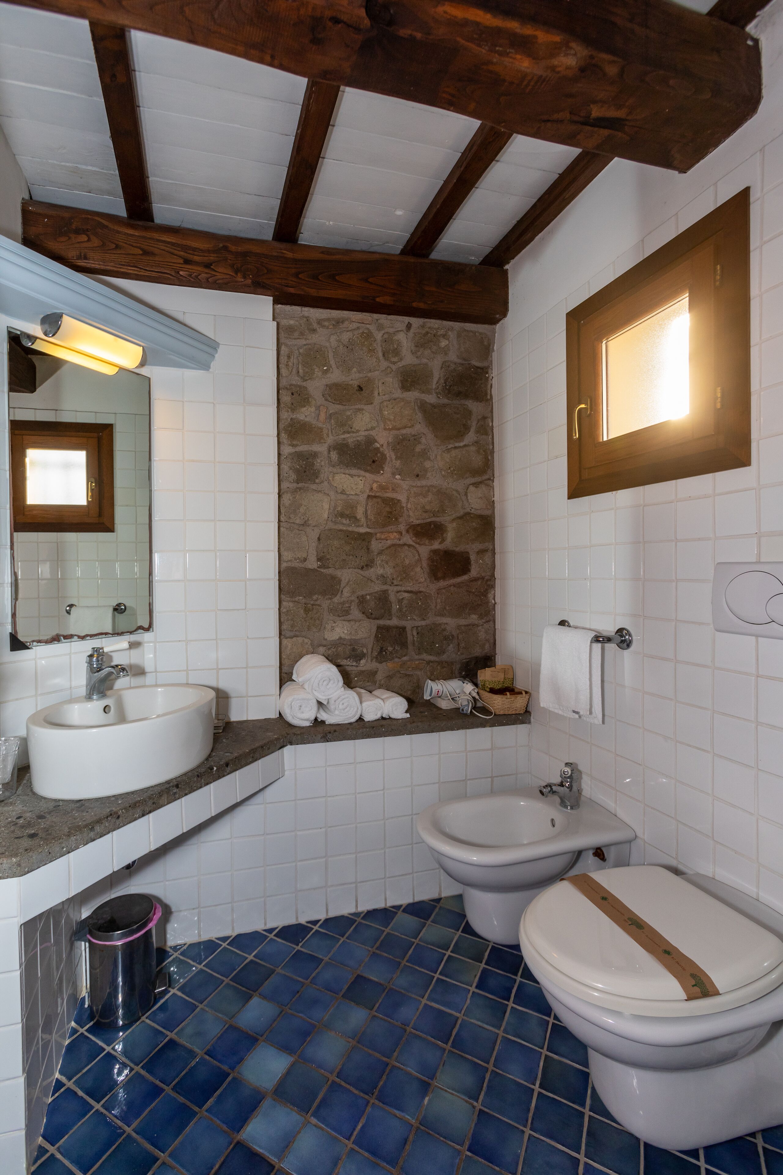A bathroom with a stone wall, a sink, a bidet, and a toilet.
