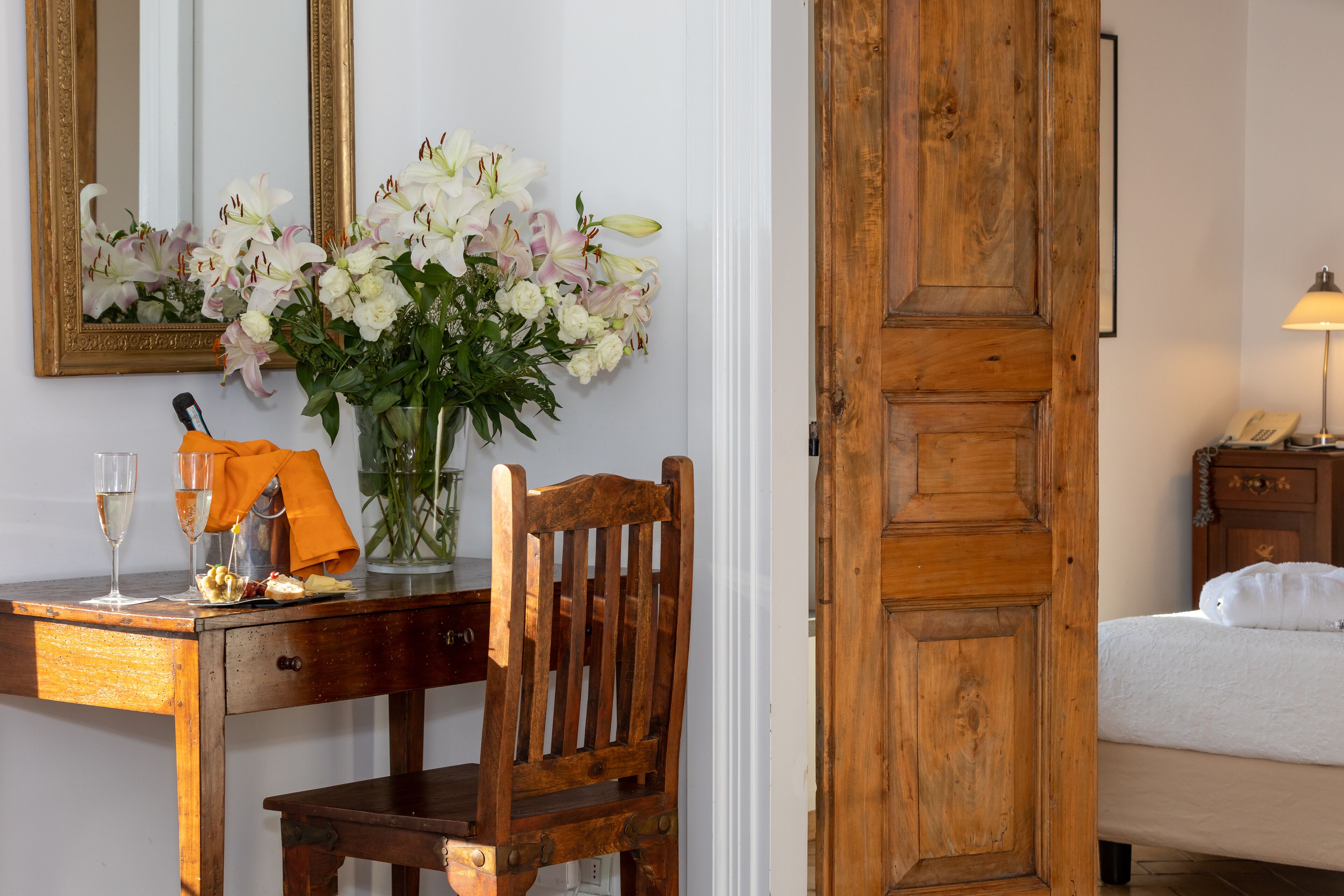 A wooden desk with a vase of flowers, a chair, and a bed with a wooden door.