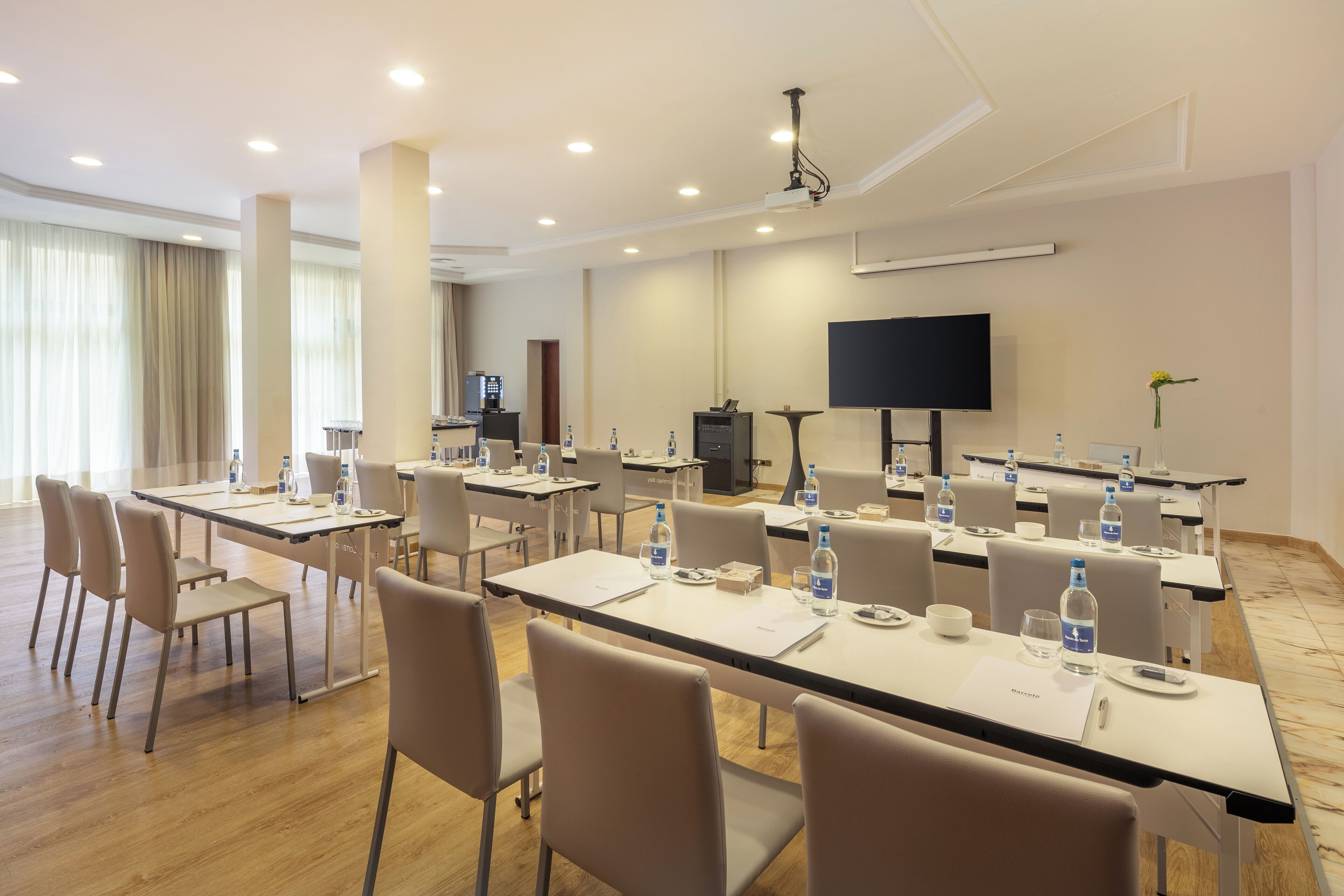 Un salón de conferencias con varias mesas, sillas y una televisión de pantalla plana en la pared.