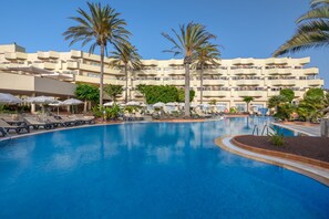 Een hotel met een groot zwembad, palmbomen en ligbedden.