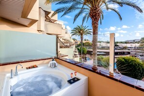Een moderne badkamer met een groot bad, een douchecabine met glazen wanden en uitzicht op een zwembad en palmbomen.