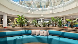 Un hall d’entrée moderne avec un canapé bleu, des palmiers et un plafond en verre.