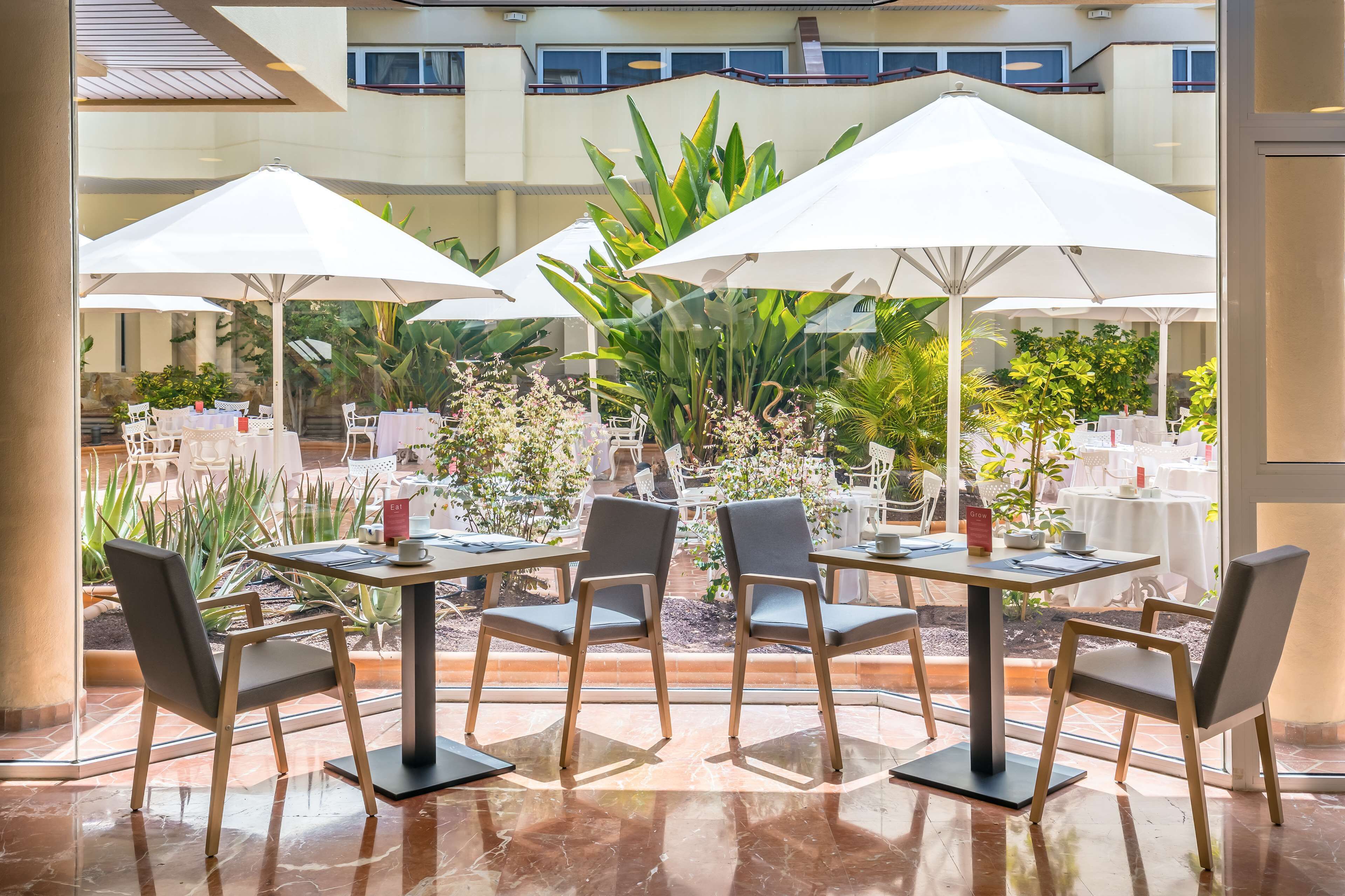 A restaurant with outdoor seating, white umbrellas, and a view of the courtyard.