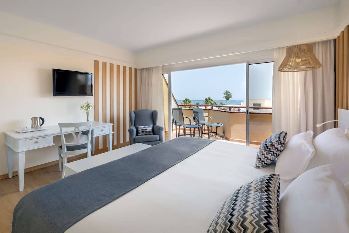 A hotel room with a bed, a desk, a chair, a TV, and a balcony with a view.