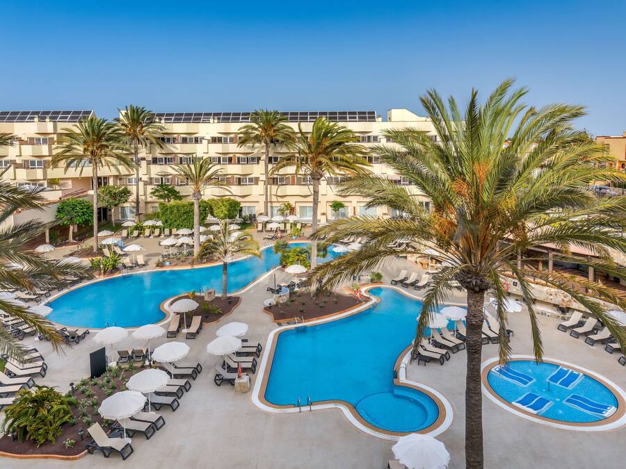 Un hotel con un amplio área de piscina, múltiples sillas de descanso y palmeras.