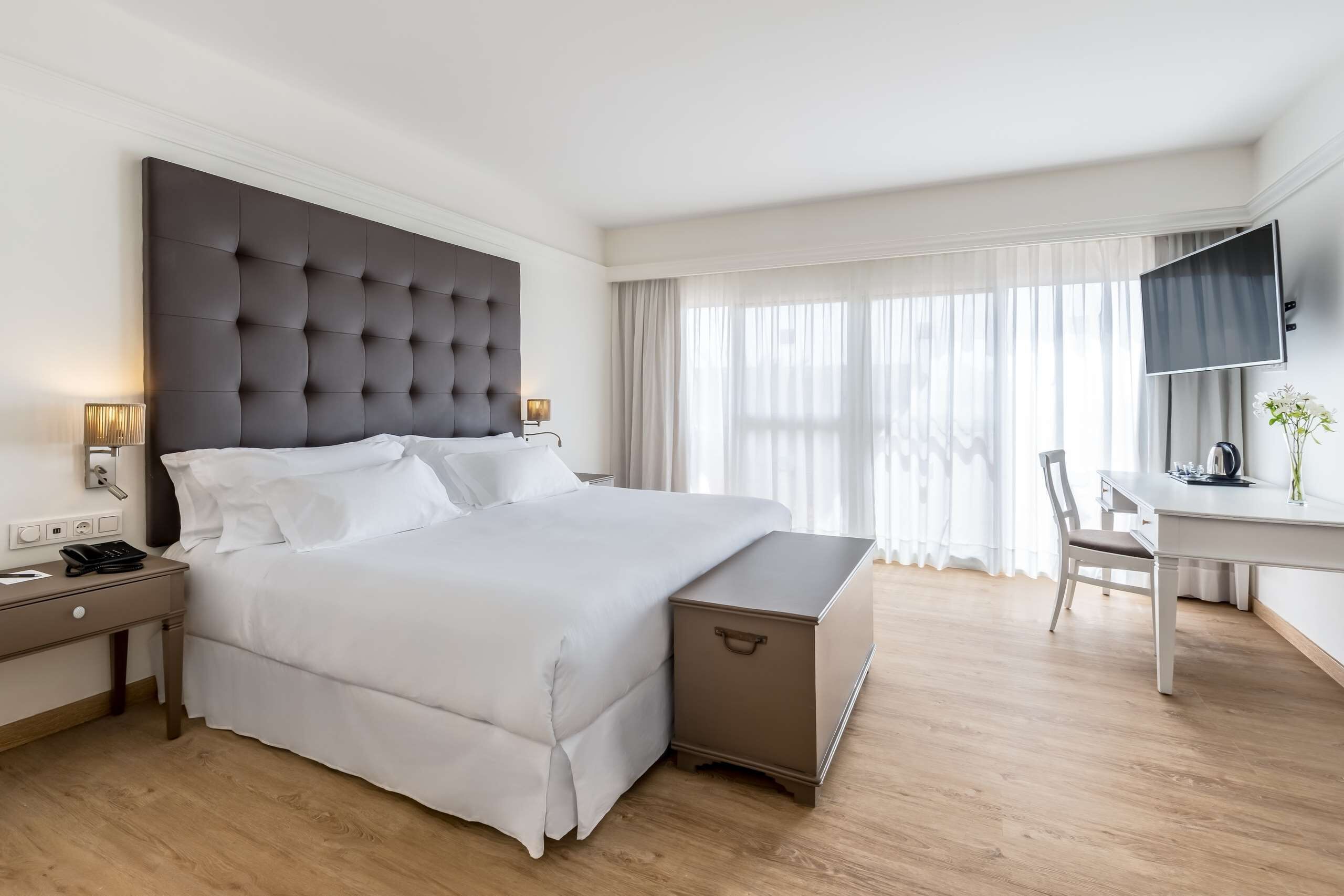 Una habitación de hotel con una cama grande, mesitas de noche, un escritorio y un televisor.