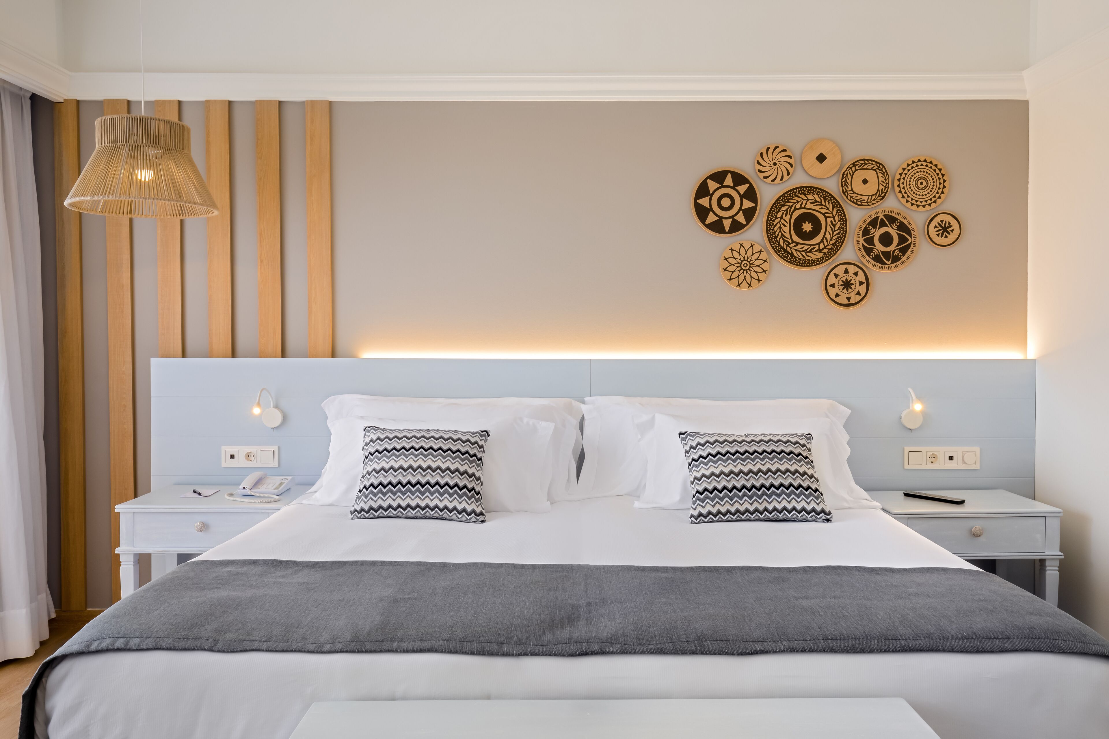 Un dormitorio ordenado con una cama, mesitas de noche y un muro decorado con diseños circulares.