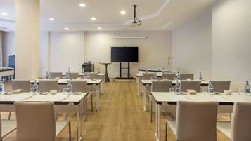 A conference room with tables, chairs, water bottles, and a television screen.