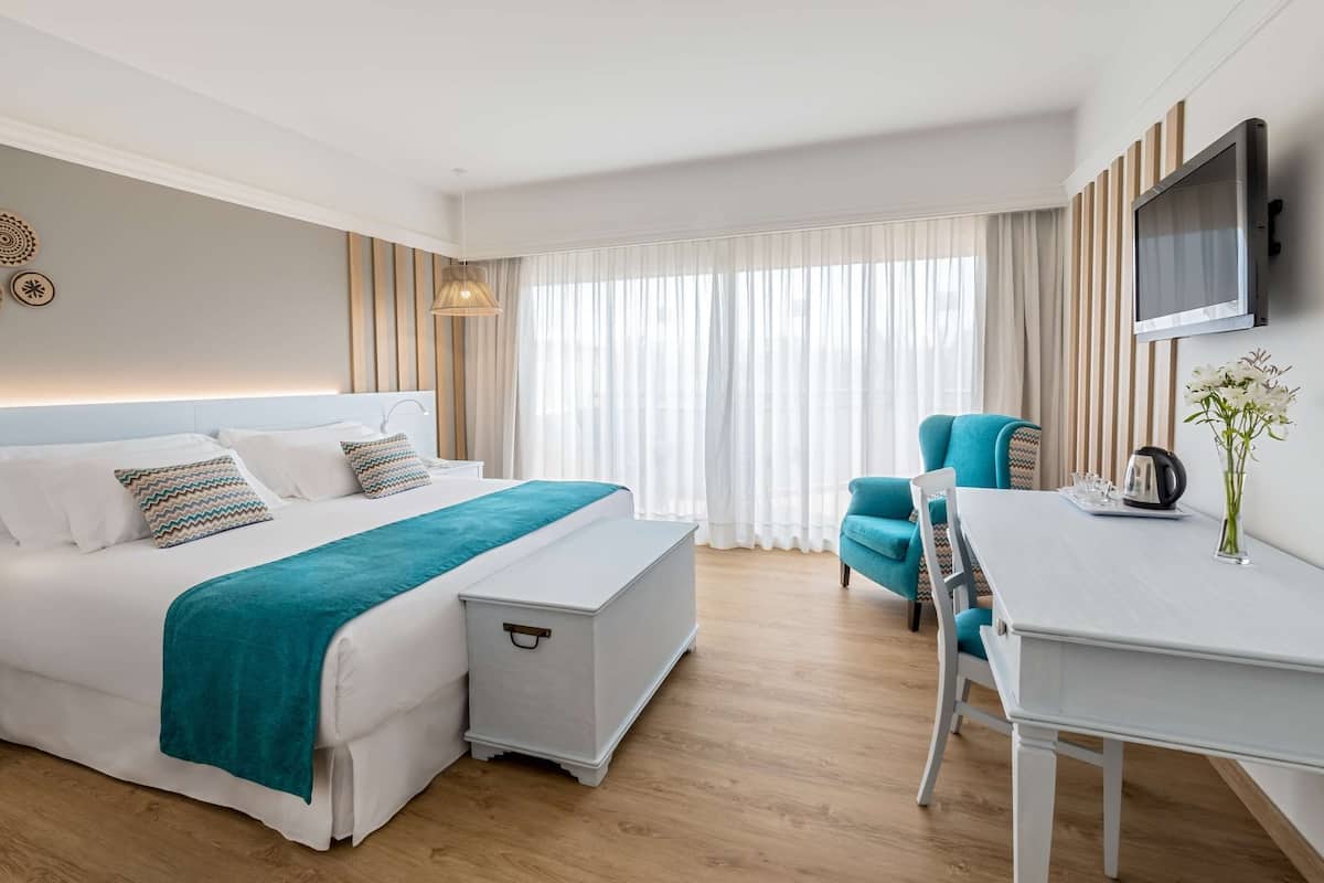 A modern hotel room with a large bed, a desk, a chair, and a TV.