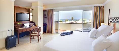 A hotel room with a bed, a desk with a laptop, a TV, and a view of the ocean.