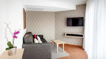A modern living room with a grey sofa, a flat-screen TV mounted on the wall, a small wooden table, and a potted orchid.