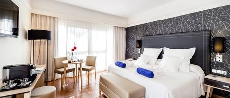 A hotel room with a bed, bedside table, desk, chair, and a TV.
