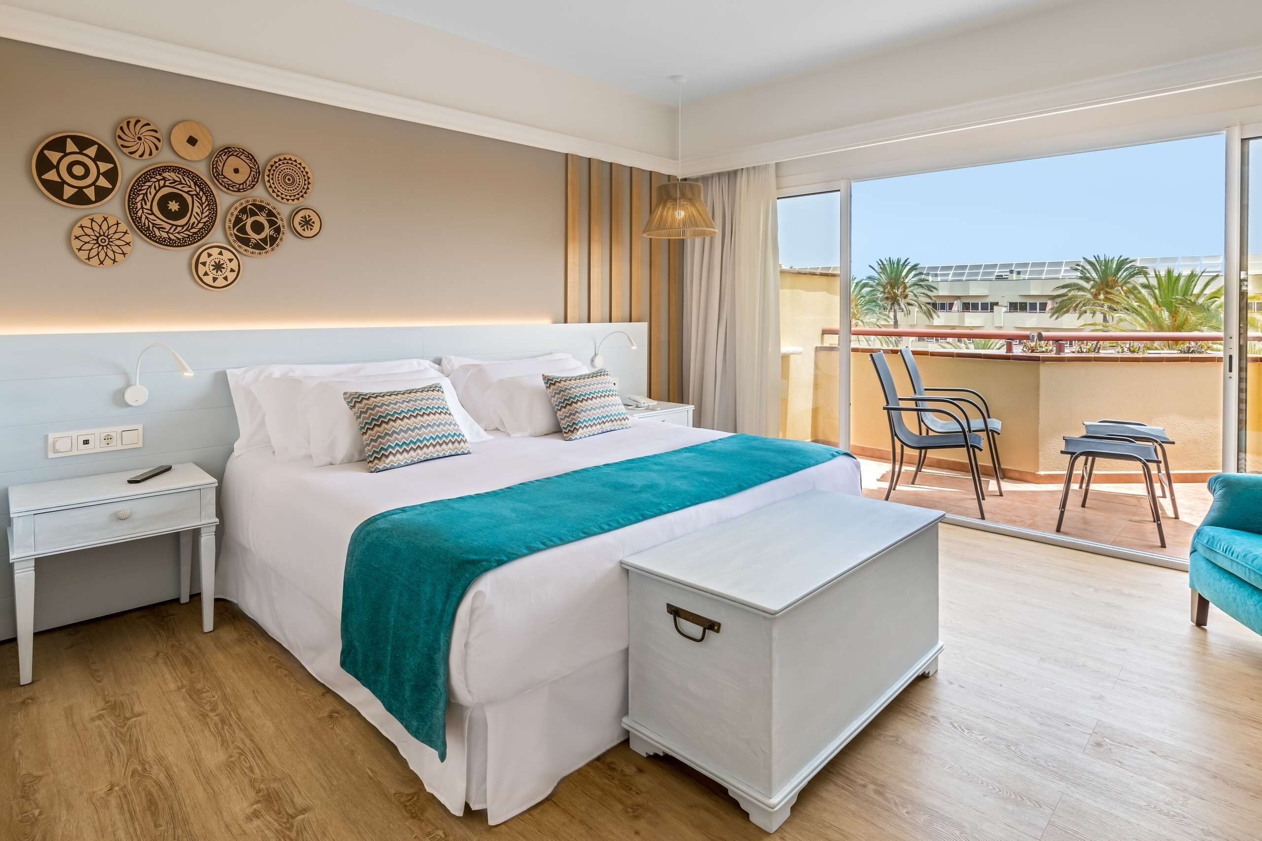 Une chambre d’hôtel moderne dotée d’un grand lit, d’une table de chevet, d’une commode, d’un balcon avec des chaises et d’une vue sur la ville.