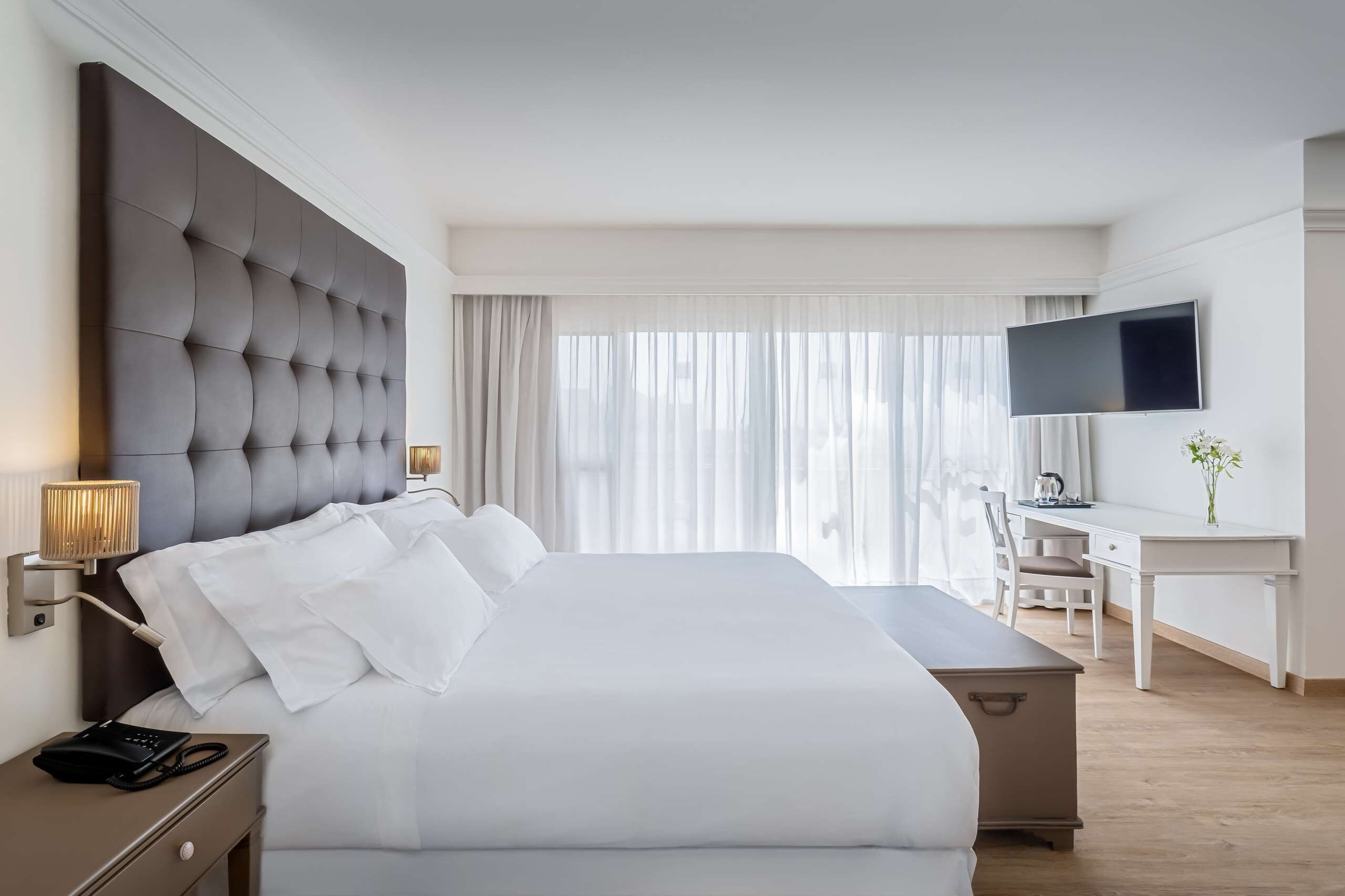 A hotel room with a large bed, a desk, a television, and a lamp.