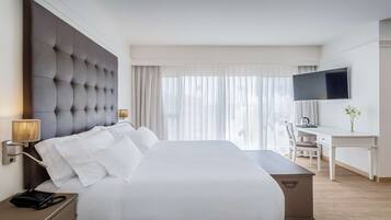 A hotel room with a large bed, a desk, a television, and a lamp.