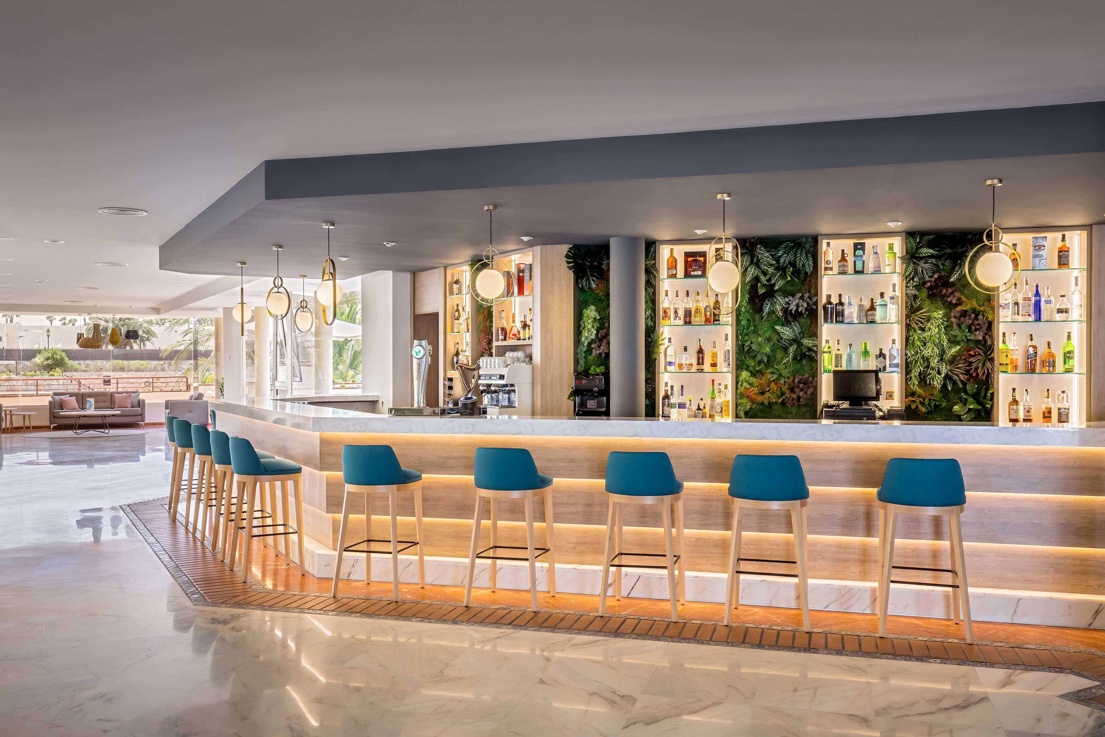 A modern bar area with a marble floor, blue bar stools, and a long counter with shelves of bottles.