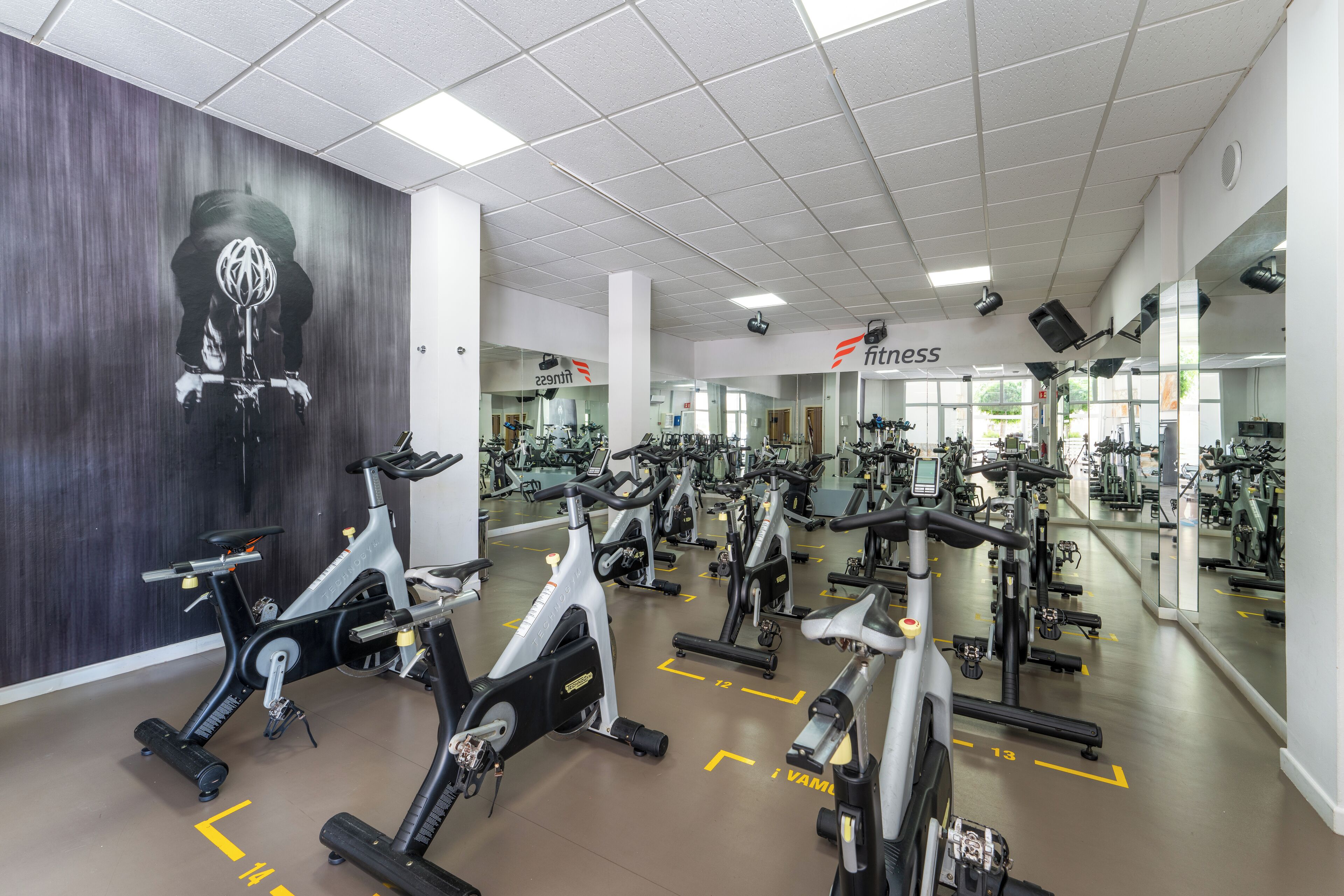 A gym with multiple exercise bikes, mirrors, and a large wall mural.