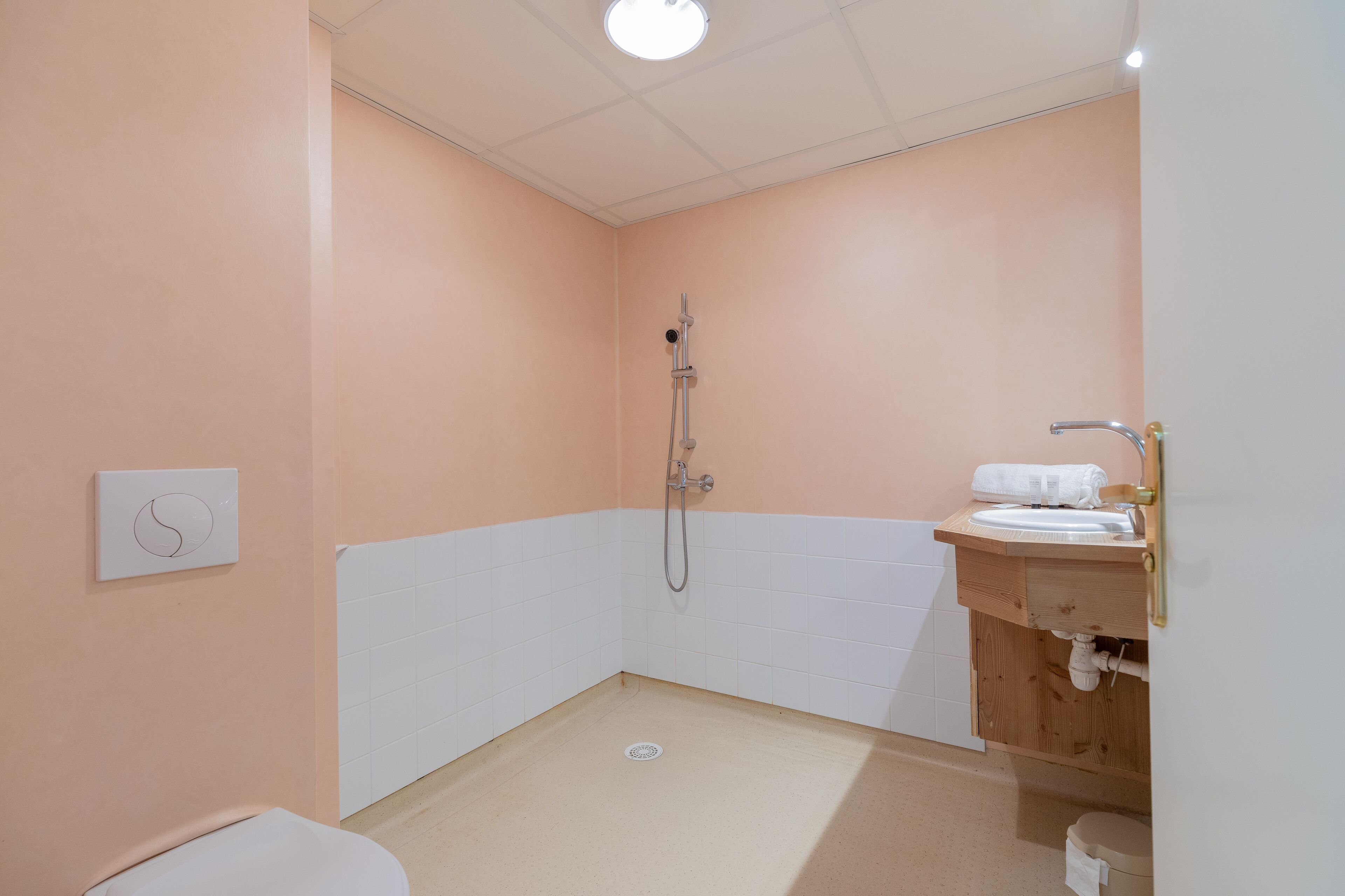 A bathroom with peach walls, white tiles, a shower, a sink, and a toilet.
