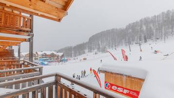 Un balcón de madera con vistas a una pista de esquí nevada, un edificio de madera y un cartel rojo con el texto 'ESF'.