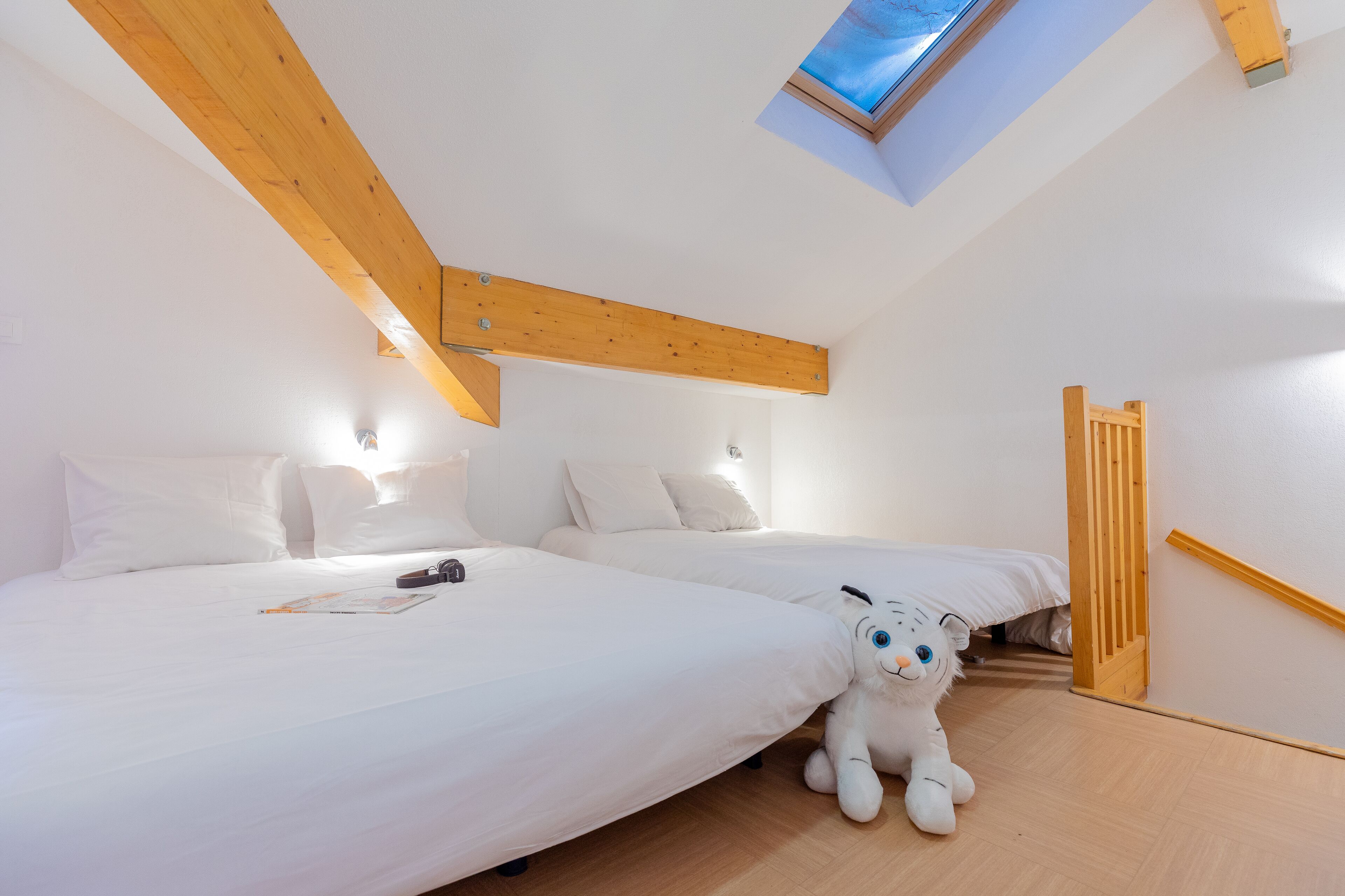 Een slaapkamer met twee bedden, houten balken, een dakraam en een knuffel.