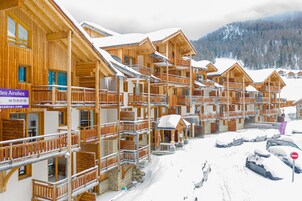 Un hôtel de style chalet en bois, doté de nombreux balcons et offrant une vue sur un paysage montagneux enneigé.
