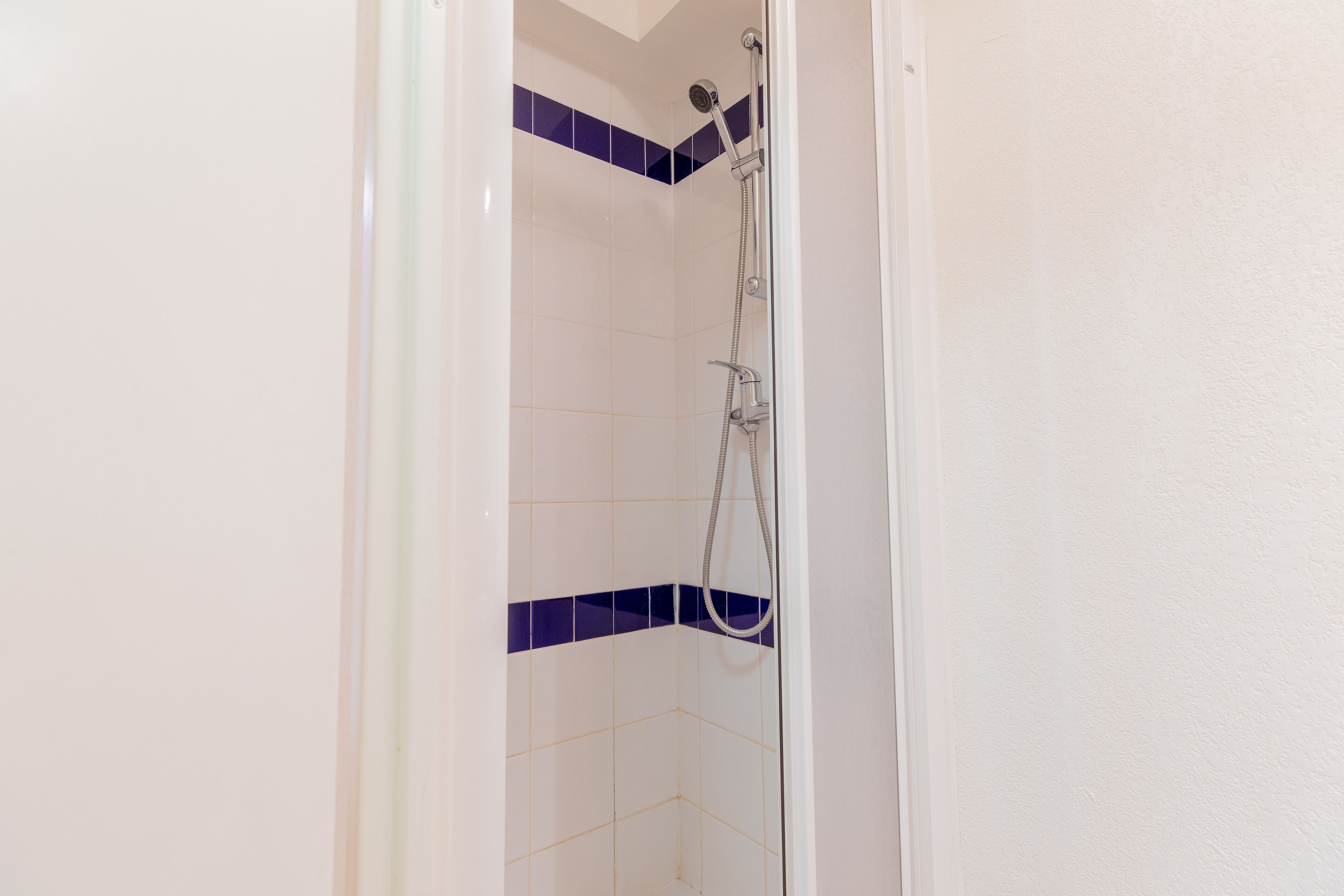 A shower with white tiles and a purple accent wall.