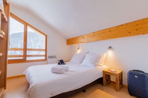 Une chambre d’hôtel avec un lit, une table de chevet avec une lampe, une valise et une fenêtre donnant sur des arbres.
