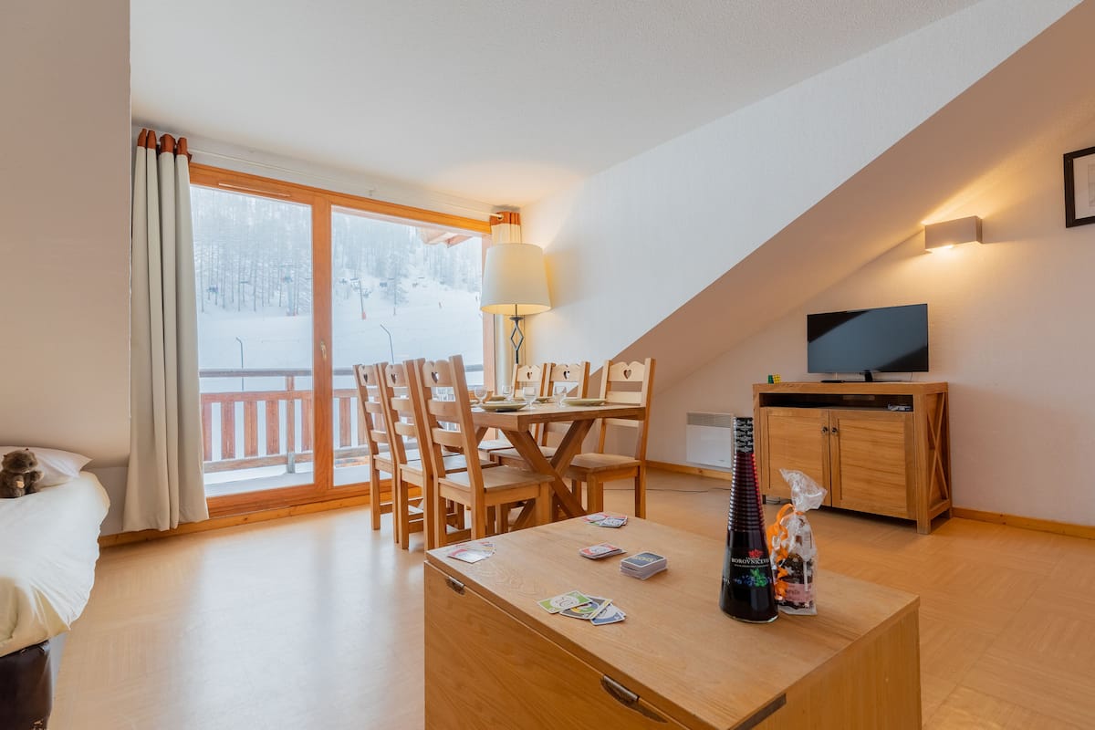 A cozy room with a dining table, chairs, a TV, and a bottle on a wooden cabinet.