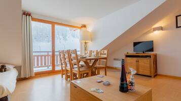 A cozy room with a dining table, chairs, a TV, and a bottle on a wooden cabinet.
