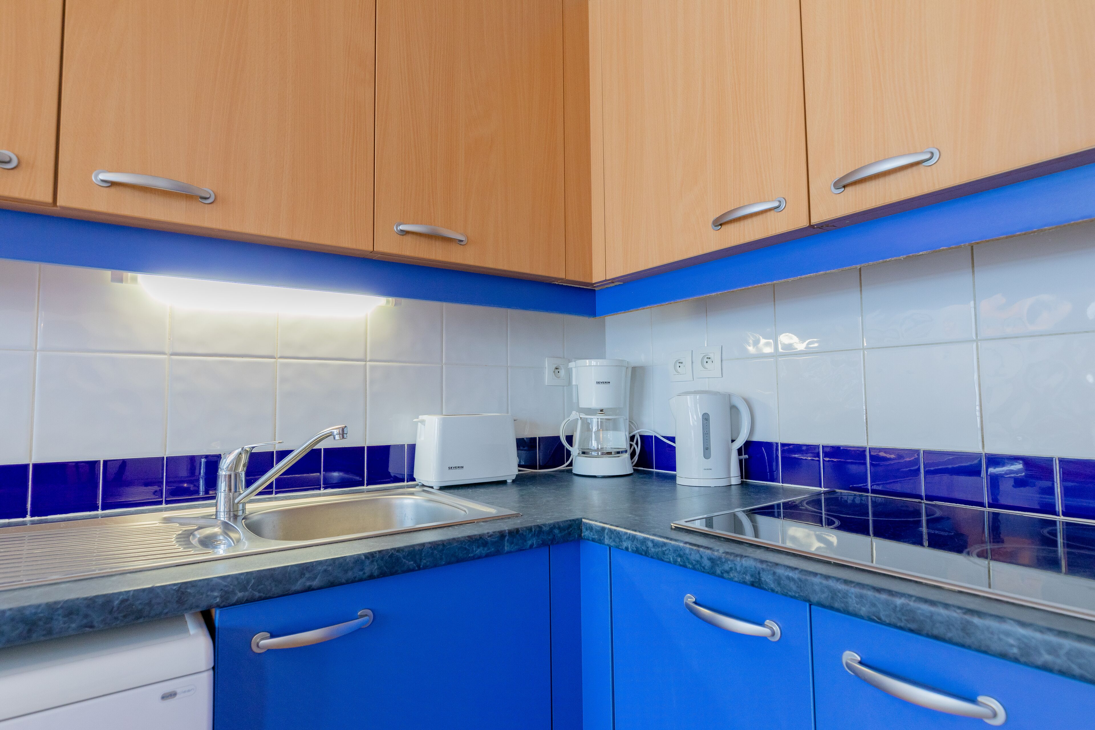 Eine Küche mit blauen Schränken, einer Edelstahlspüle und weißen Geräten, darunter eine Kaffeemaschine und ein Toaster.