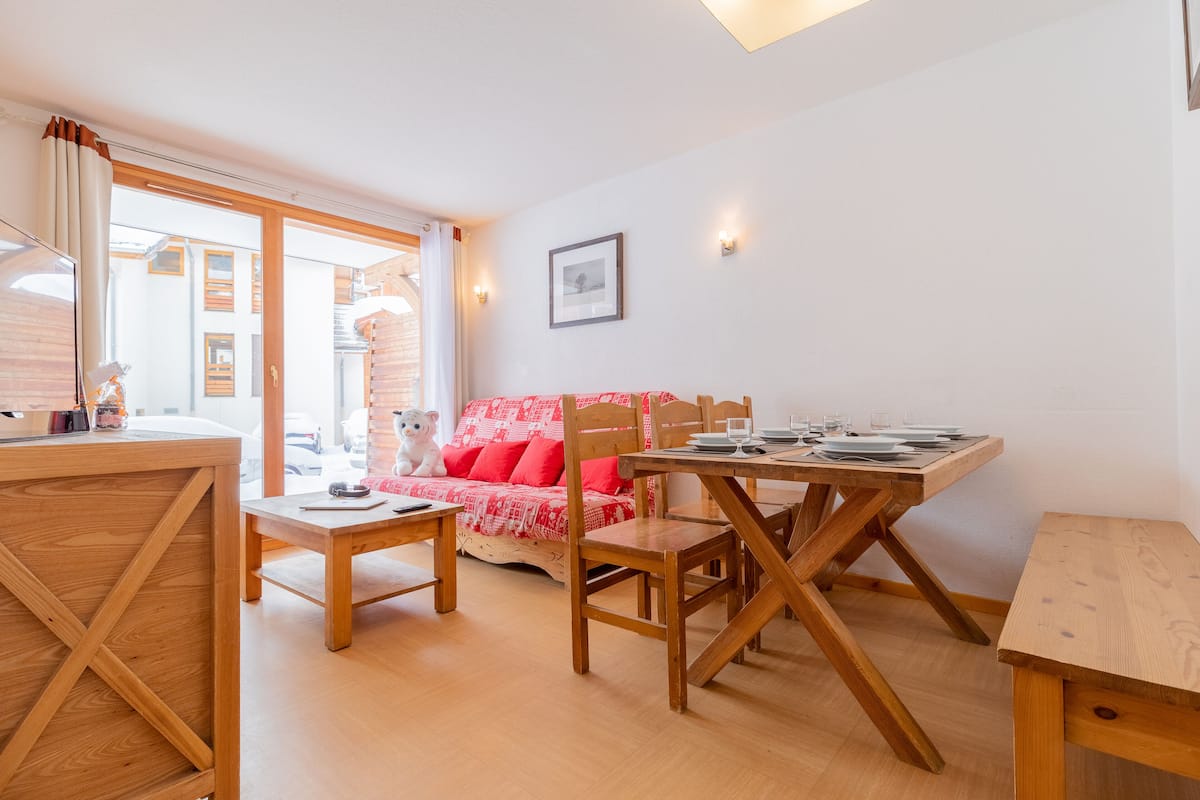A cozy room with a wooden dining table, chairs, and a sofa with red cushions.