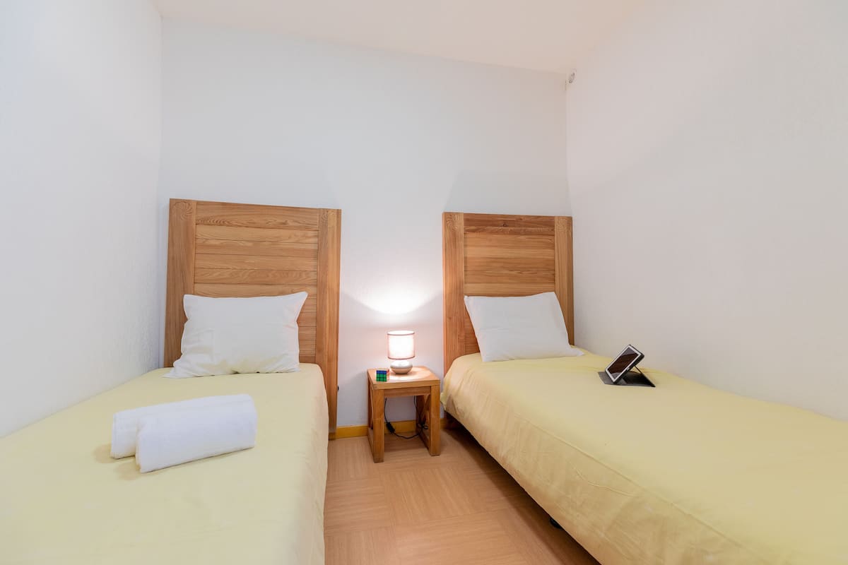 A small, clean room with two single beds, a bedside table with a lamp, and a mobile phone on the right bed.