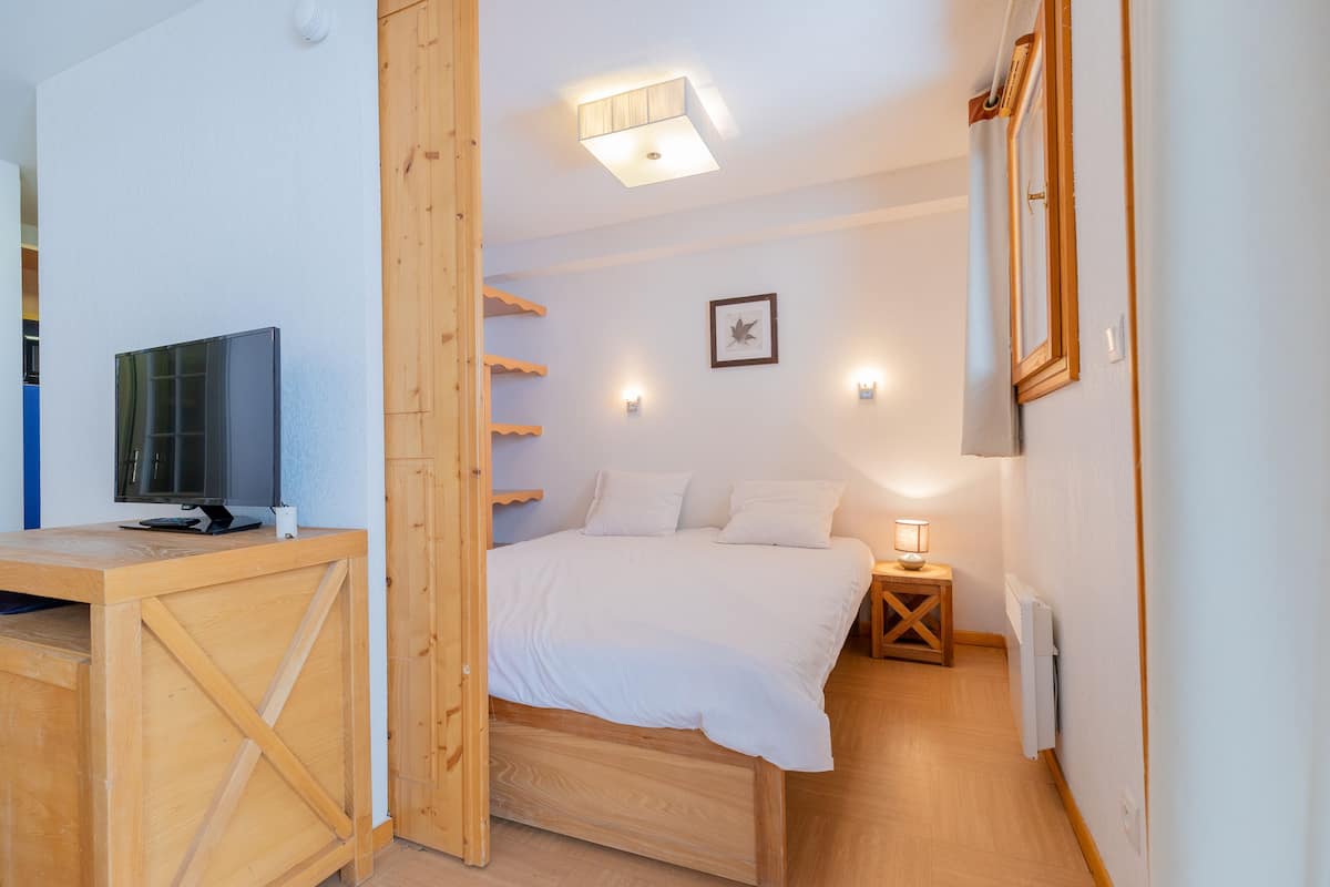 A bedroom with a bed, bedside table, lamp, and a television on a desk.