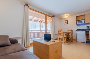 Un salon chaleureux avec un canapé marron, un bureau en bois avec un ordinateur portable et un coin repas comprenant des chaises et une table en bois.