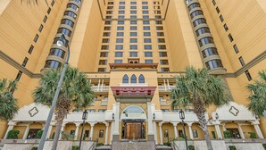Un hôtel à plusieurs étages doté d’une entrée principale, de balcons et de palmiers.