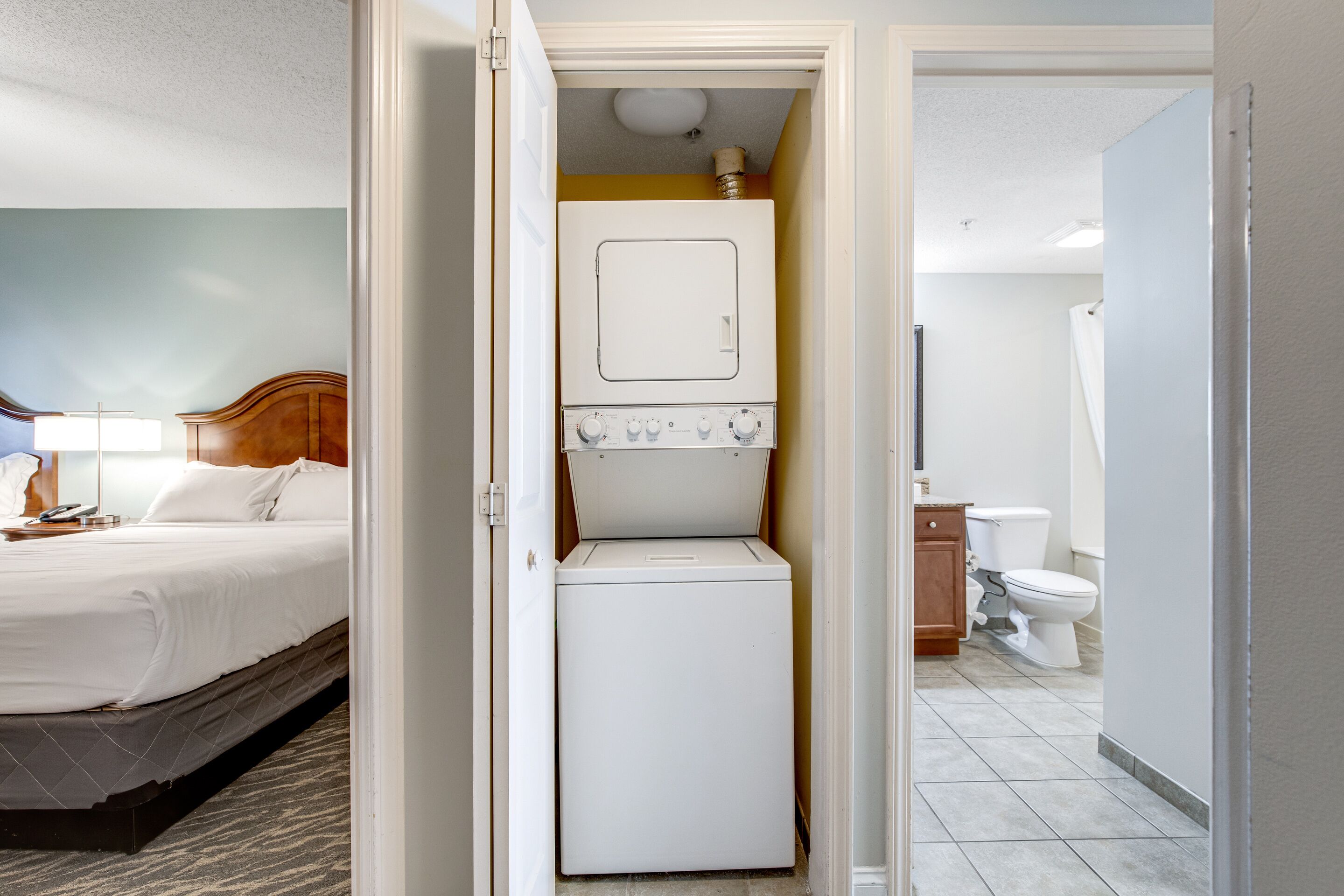 A hotel room with a bed, a washing machine, a toilet, and a shower area.
