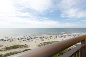 A beach with umbrellas and people, viewed from a balcony.