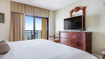 A hotel room with a large bed, a wooden dresser, a television, and a balcony with a chair.