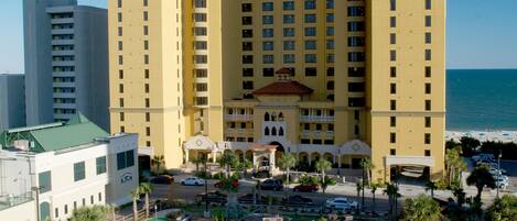 A large hotel with multiple floors, a parking area, and a pool complex.