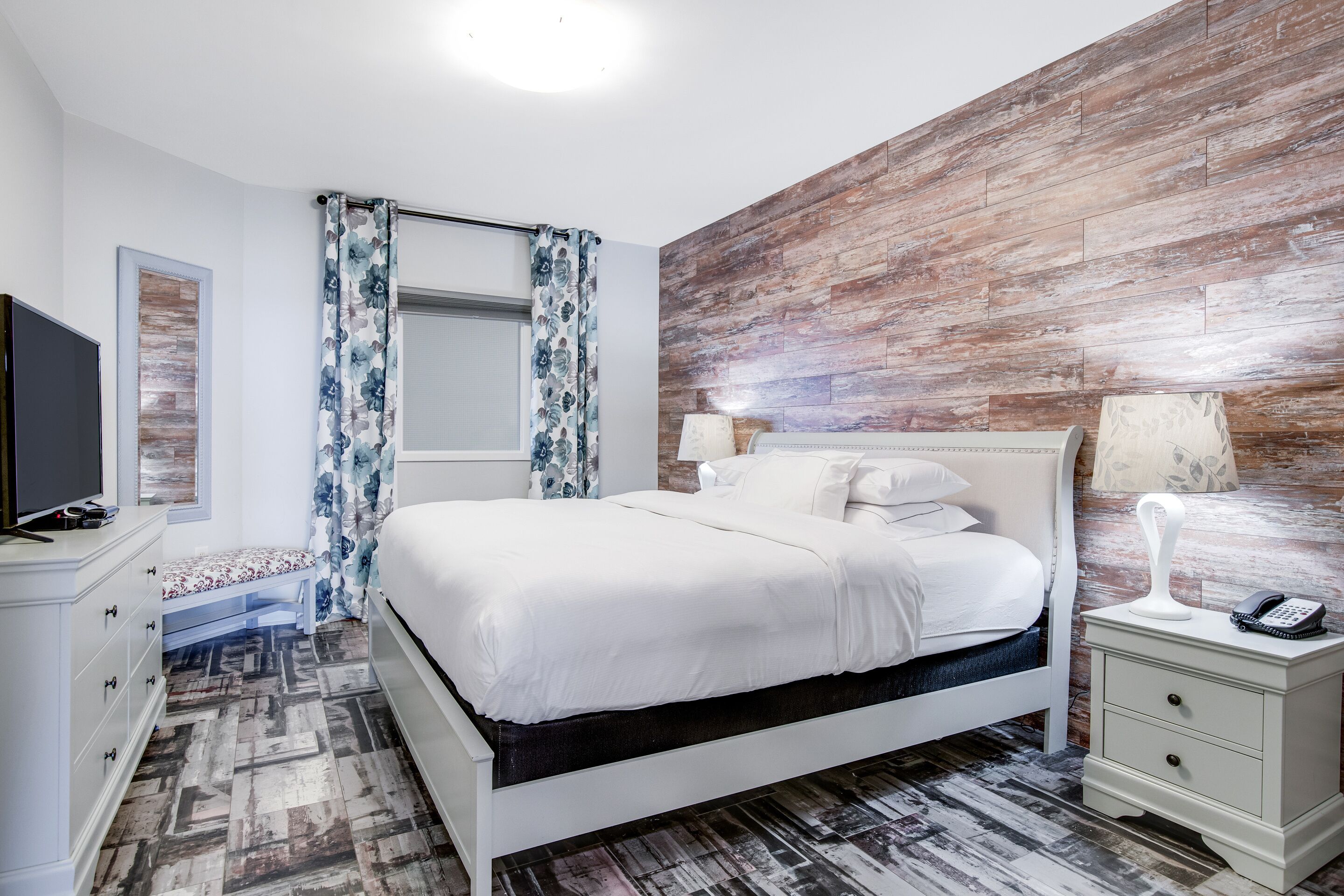 A bedroom with a bed, bedside tables, a TV, and a bench.